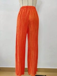 Detail of high-waist pleated wide-leg pants in bright orange with elastic waistband