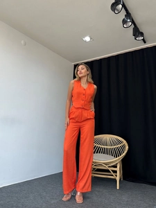 Detail of orange linen two-piece set featuring V-neck button vest and wide-leg trousers