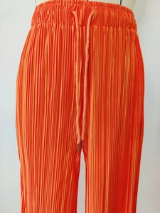 Close-up of bright orange pleated trousers with elastic drawstring waist and metal aglets