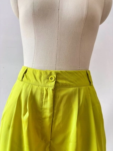 Detail of high waist neon green trousers with pleated waistline and matching button
