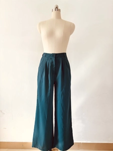 Detail view of high waisted pleated wide leg pants in dark teal with button closure