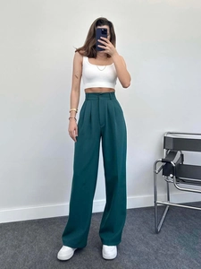 Full view of high waisted dark green wide leg trousers styled with white top and sneakers