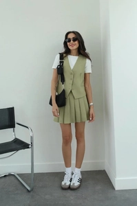 Detail view of the sage green vest and pleated mini skirt set in a modern urban style