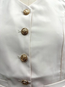 Close-up of luxury cream twill fabric with ornate gold crest buttons on a two-piece set