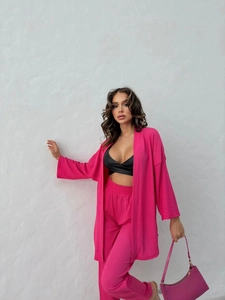 Detail of bright pink two-piece set featuring long cardigan and high-waisted trousers