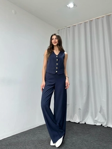 Detailed view of dark blue V-neck vest with golden buttons and wide-leg trousers