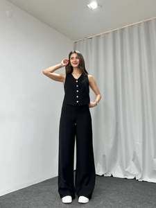 Detail of tailored black vest with white buttons and high-waisted wide-leg trousers