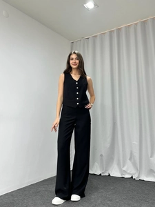 Detail view of black sleeveless vest with white buttons and matching wide leg trousers