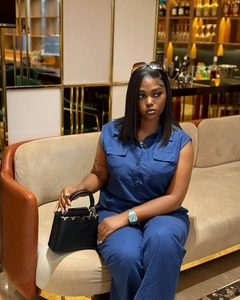 Detail view of a blue sleeveless jumpsuit with flap chest pockets and a chic black handbag