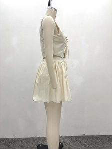 Détail du gilet à nouer et de la jupe plissée aux bords festonnés en crème