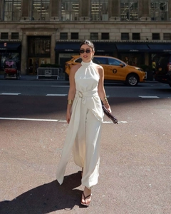 Detail eines eleganten beigen Neckholder-Jumpsuits mit Metallgürtel und Plissee-Struktur