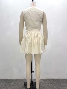 Détail de l'ourlet ondulé sur la jupe plissée taille haute et le haut gilet crème