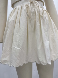 Détail de la jupe plissée crème à taille haute avec cordon et ourlet festonné brodé