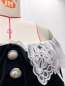 Détail de l'encolure en dentelle florale blanche et des boutons en perles sur robe noire