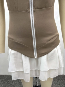 Détail d'un gilet marron avec fermeture éclair et mini-jupe blanche à volants étagés
