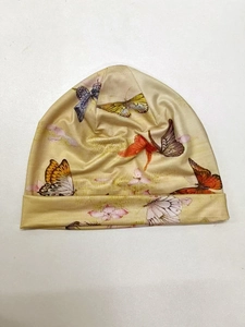 Dettaglio ravvicinato del berretto in maglia con stampa di farfalle e fiori su tessuto beige