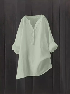 Loose fit linen V-neck women shirt in light green hanging on a dark wood background
