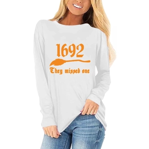 Détail du motif sorcière de Salem sur T-shirt blanc manches longues avec texte orange et balai