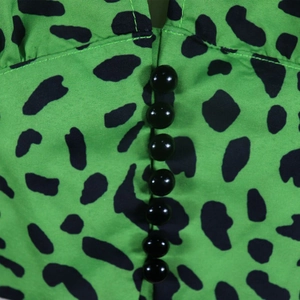 Detail of leopard print fabric in green with black buttons and fine woven texture