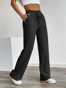 Detail of high-waist black wide-leg pants featuring textured fabric and drawstring waist