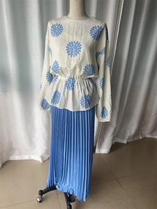 Detail of white long-sleeve top with floral prints and a pleated light blue maxi skirt