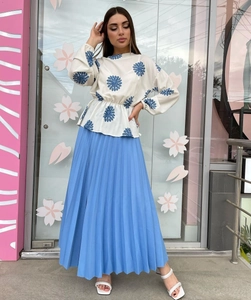Detail of white long-sleeve embroidered top paired with a light blue pleated chiffon skirt