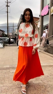 Detail of floral long-sleeve top and orange pleated midi skirt set for women
