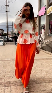 Detailed texture of white floral long-sleeve top and high-waist orange pleated skirt