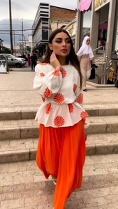 Detail of pleated orange skirt and patterned long sleeve blouse in outdoor urban setting