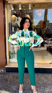 Detail of elegant white long-sleeve shirt with green abstract print and high-waist pants