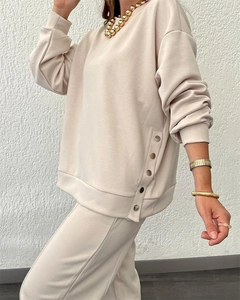 Detail view of beige tracksuit top featuring stylish metal buttons on the side split hem