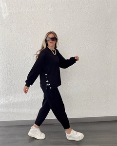 Detail of black tracksuit featuring metallic side buttons on the long sleeve sweatshirt