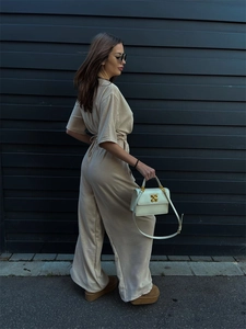 Detailed close-up of the beige pleated fabric texture and drawstring waist on the jumpsuit