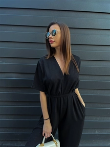 Detail of black V-neck jumpsuit with waist tie and textured woven fabric with pockets