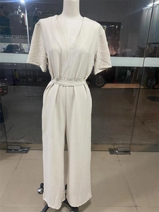 Detail of apricot V-neck jumpsuit showing belted waist and pleated fabric texture