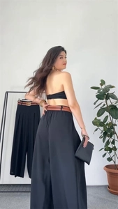 Detail of high waisted black wide leg trousers with brown leather belt and pleated front