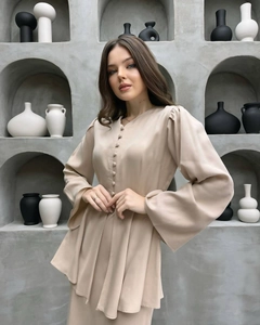 Dettaglio elegante top beige con scollo a V, bottoni in tessuto e ampie maniche a campana