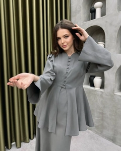 Dettaglio del cardigan grigio con scollo a V, bottoni foderati e orlo a balze elegante