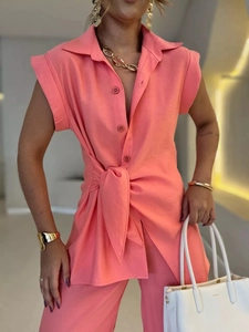 Détail de chemise sans manches rose corail avec col à revers, boutons et nœud à la taille