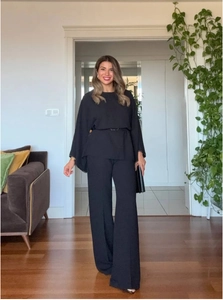 Detail of black two-piece set featuring a belted cape top and wide-leg trousers