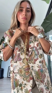 Détail d'un collier en Y doré à glands et bracelets superposés sur un blazer à fleurs