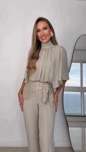 Detail of high-neck pleated top and straight trousers with a golden woven belt