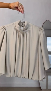 Detail of high neck pleated chiffon top in beige with elegant lantern sleeve texture