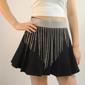 Detail of black pleated mini skirt featuring a wide rhinestone belt and shimmering fringe