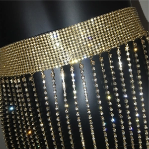 Detail shot of golden rhinestone body chain featuring long fringe tassels on black base