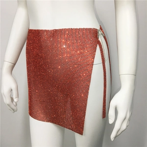Détail d'une jupe en maille strassée orange avec fente latérale et chaîne métallique