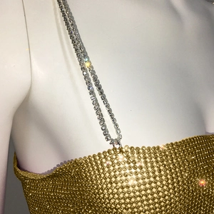Détail d'un haut en maille dorée avec de doubles bretelles ornées de strass brillants