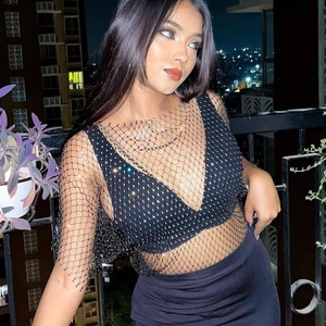 Sparkly black rhinestone fishnet mesh top worn by a model against a night city background