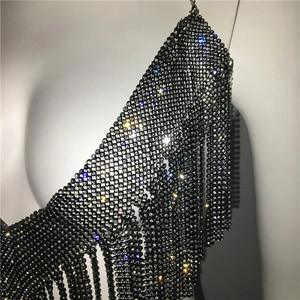 Détail d'un haut en maille métallique noire orné de strass brillants et de fines franges
