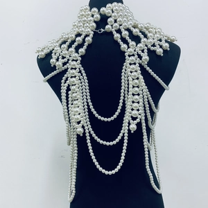 Detailed close-up of layered white pearl body chain and shoulder jewelry on a black bust
